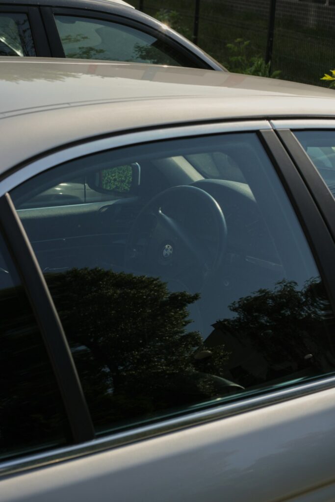 Driver sits in a parked vehicle with tinted side windows, reduced dashboard glare, and sunlight across the cabin.