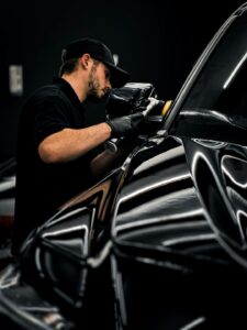 A driver inspecting bubbled window tint on a parked car with a microfiber cloth nearby.